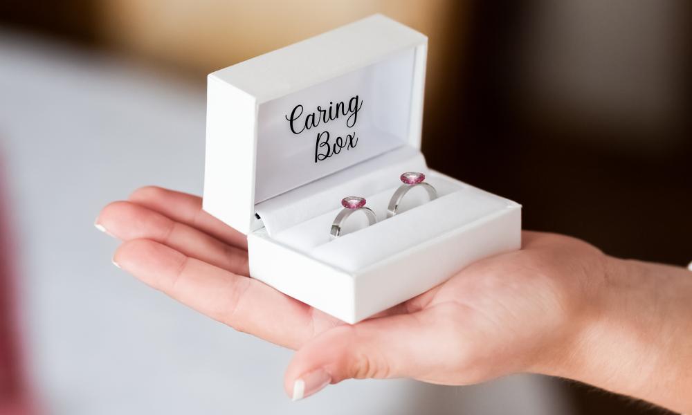 a hand holding a box with pink sapphire rings