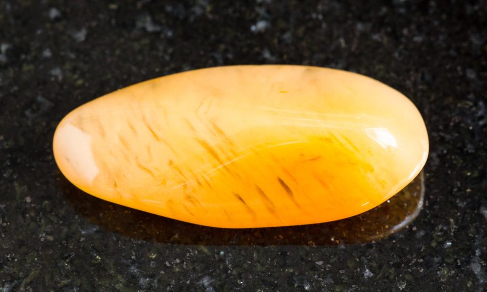 a yellow jasper oval shaped stone on a black surface
