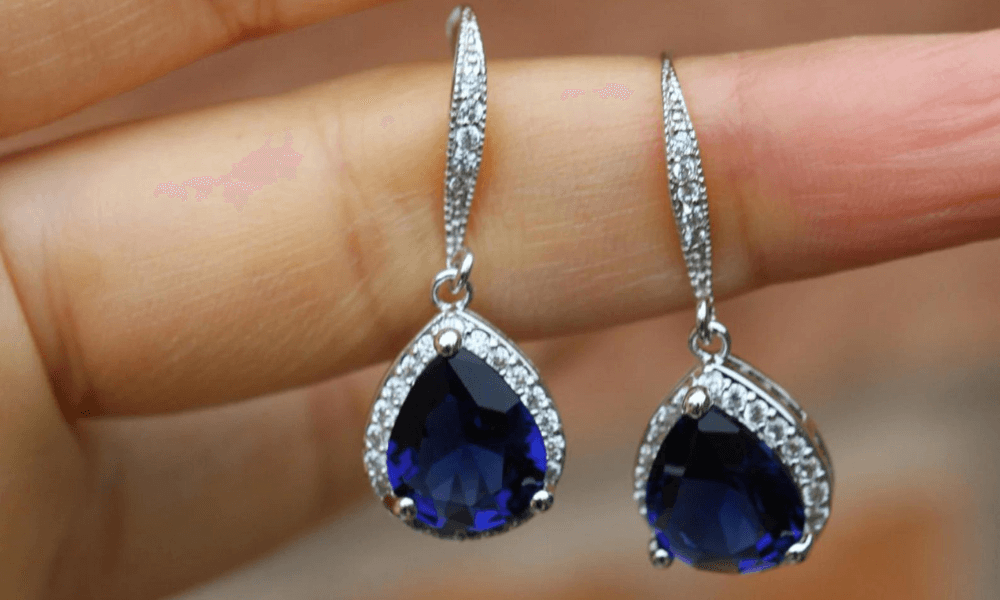 a person holding a pair of blue sapphire earrings in their hand