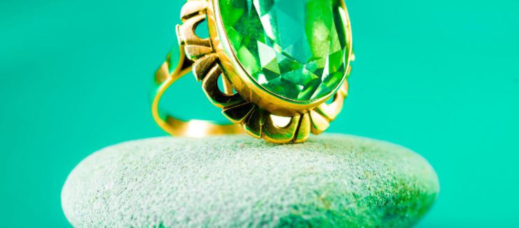 A green sapphire ring with an intricate gold setting was placed on a smooth grey stone against a vibrant green background.