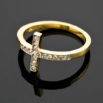 Gold ring with a cross design, adorned with small diamonds, on a reflective surface. This ring is called diamond cross ring.