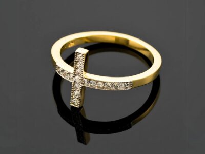 Gold ring with a cross design, adorned with small diamonds, on a reflective surface. This ring is called diamond cross ring.