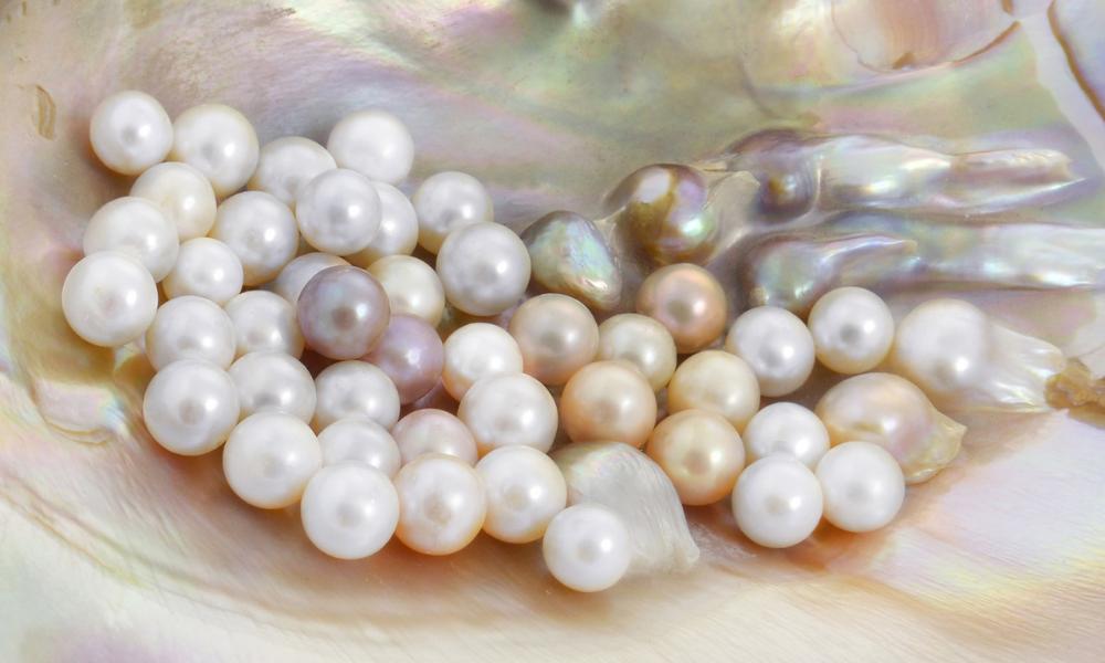 A collection of lustrous pearl stones in white and pink tones on a shiny mother-of-pearl shell background.