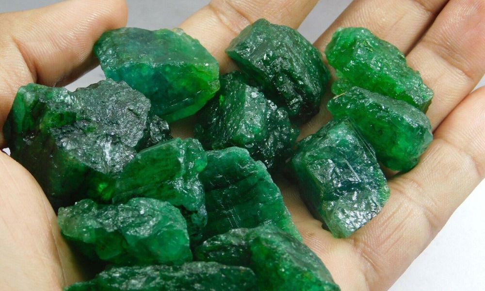 A hand holding a collection of raw emerald crystals.