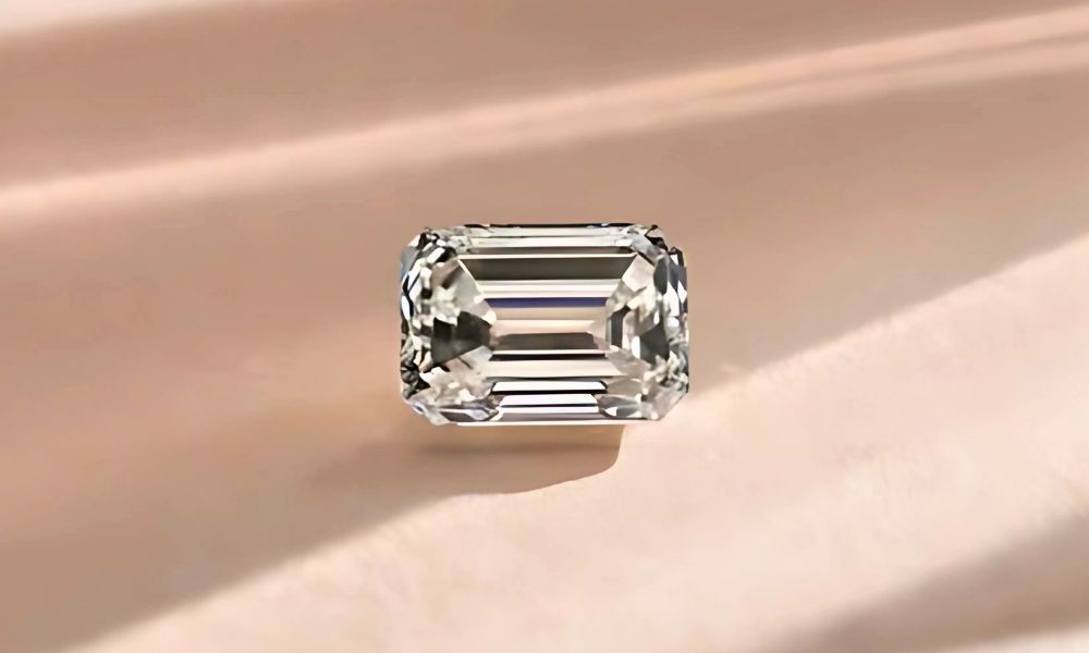 A emerald cut diamond on a soft beige surface with light reflections.