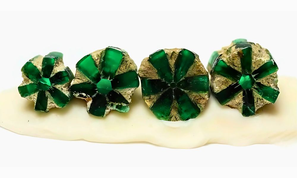 four trapiche emerald glass star-shaped stones on a white surface.