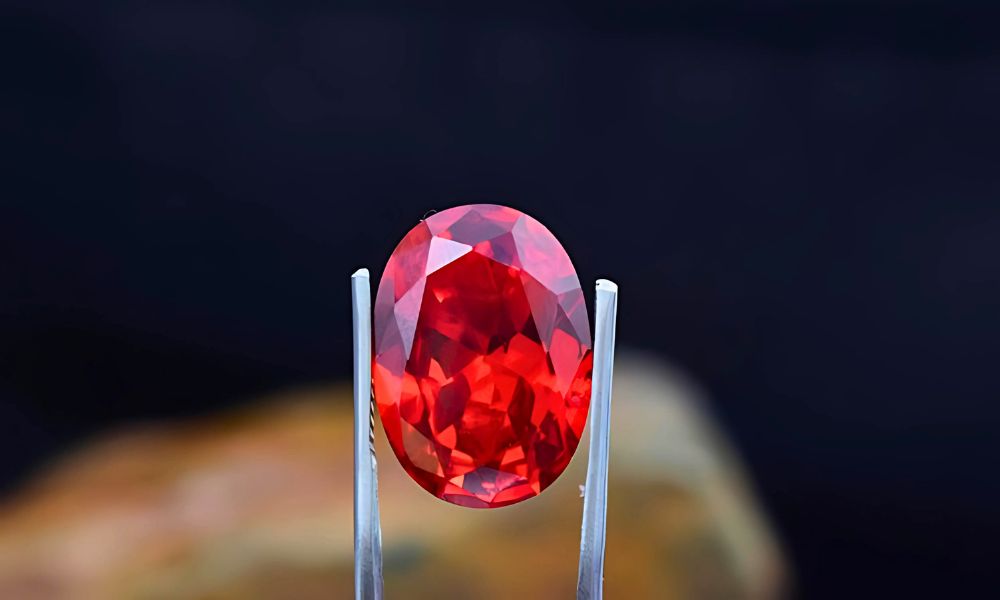 A large red emerald held by tweezers against a dark background.