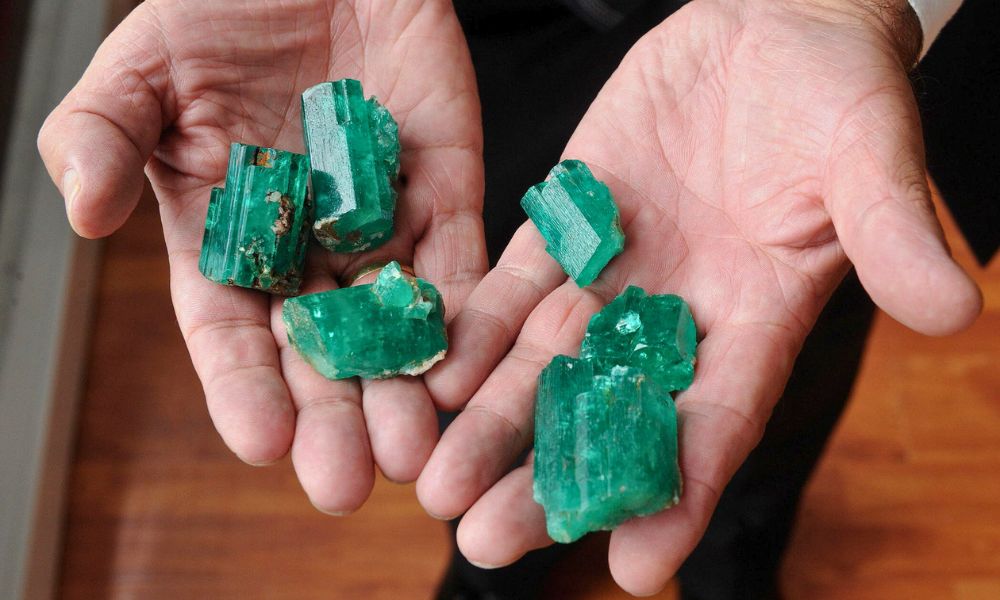 Hands holding raw emerald crystals.