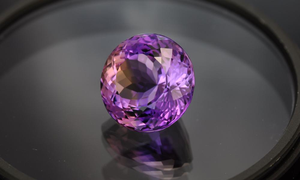 A radiant purple diamond on a reflective dark surface.