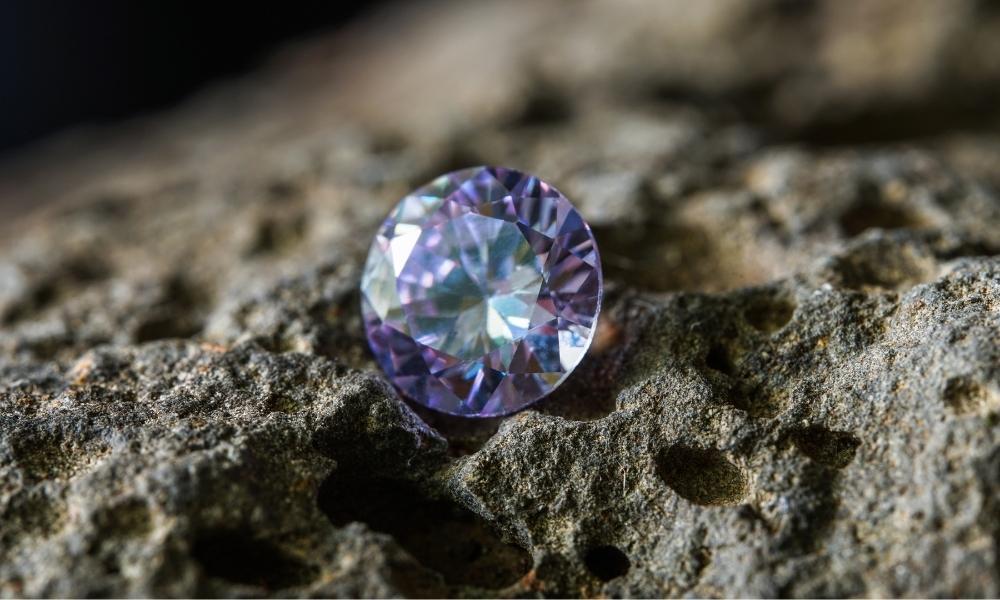 Iridescent purple diamond on a rugged rock surface.