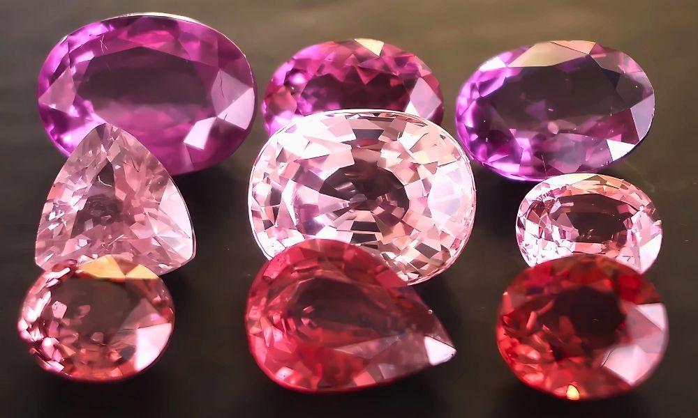 Assorted pink ruby and red and purple gemstones on a reflective surface.