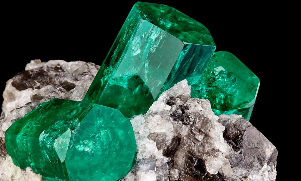 Raw emerald crystals on a bed of gray rock.