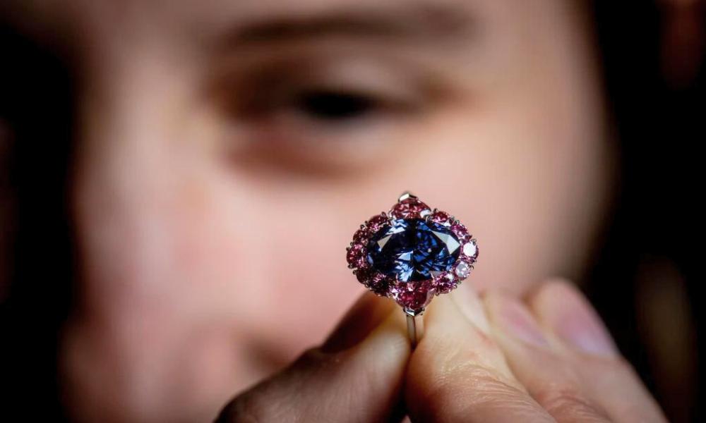 Close-up of a large purple diamond ring held in front of a person's face.