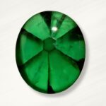 Oval-shaped, vibrant trapiche emerald with visible internal fractures, on a white background.