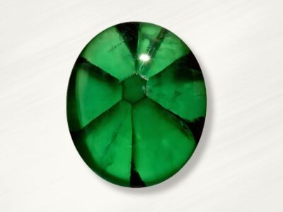 Oval-shaped, vibrant trapiche emerald with visible internal fractures, on a white background.