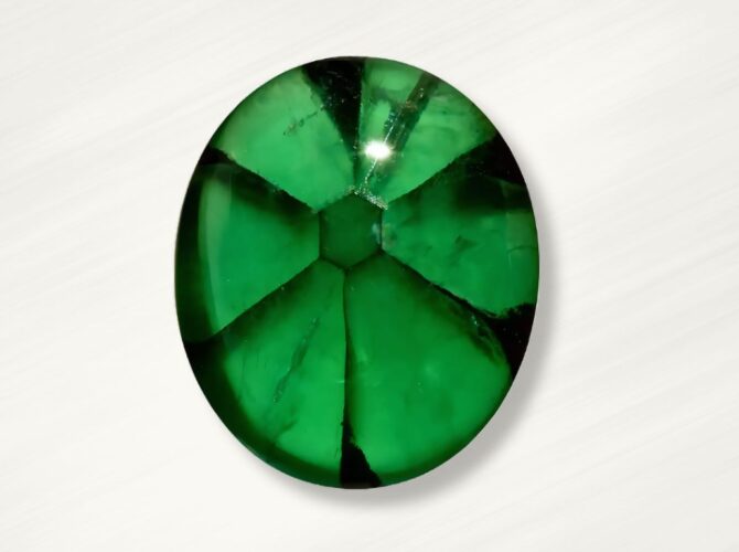 Oval-shaped, vibrant trapiche emerald with visible internal fractures, on a white background.