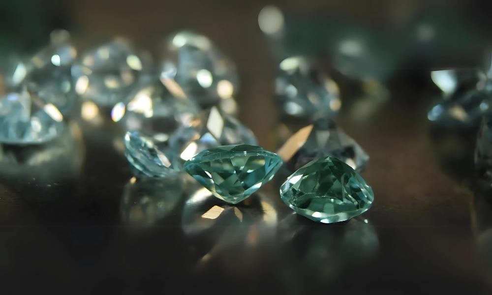 A collection of sparkling, faceted green diamonds scattered on a reflective surface.