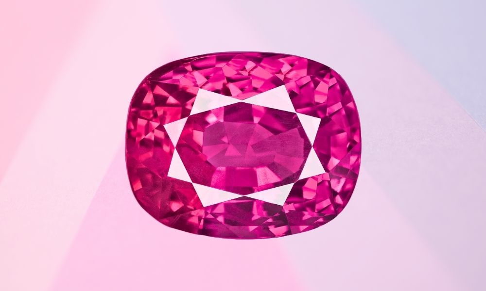 A vivid pink ruby with faceted cut placed on a dual-tone pink and purple background.