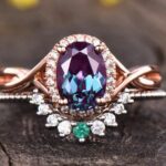 Oval-cut alexandrite rings with diamond accents on a rose gold band against a wooden backdrop.