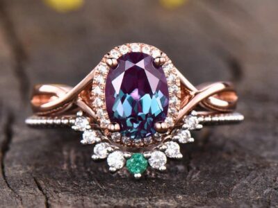 Oval-cut alexandrite rings with diamond accents on a rose gold band against a wooden backdrop.