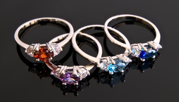 Four gemstone rings with red, purple, and blue stones on a reflective black surface.
