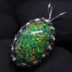 A glittering green opal wrapped in a wire setting against a dark background.