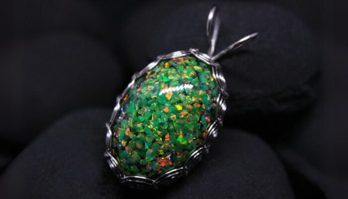 A glittering green opal wrapped in a wire setting against a dark background.