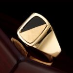 Gold and black signet mens gemstone rings on a dark wooden surface.