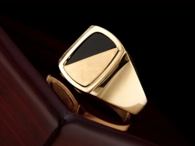 Gold and black signet mens gemstone rings on a dark wooden surface.