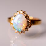 Gold ring with a large opal surrounded by smaller diamonds, on a reflective surface. This is called opal wedding rings.