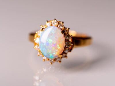 Gold ring with a large opal surrounded by smaller diamonds, on a reflective surface. This is called opal wedding rings.