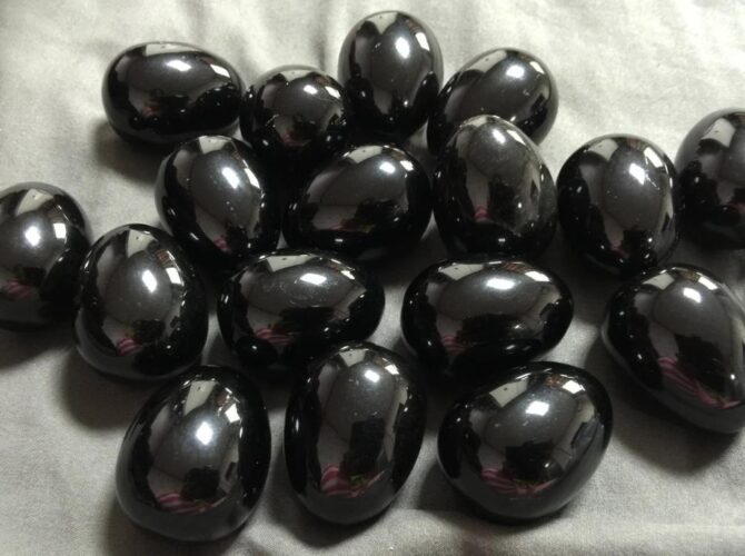 Black obsidian polished stones on a grey fabric surface.