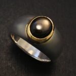 A black sapphire ring with a central black pearl set in gold on a dark background.