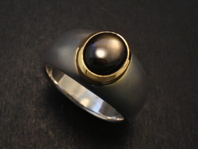 A black sapphire ring with a central black pearl set in gold on a dark background.