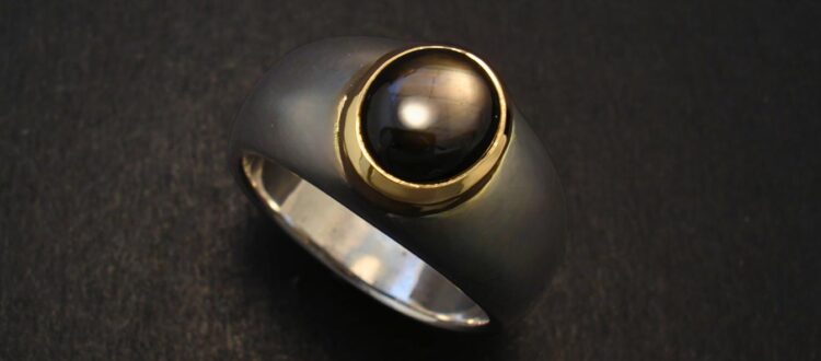 A black sapphire ring with a central black pearl set in gold on a dark background.