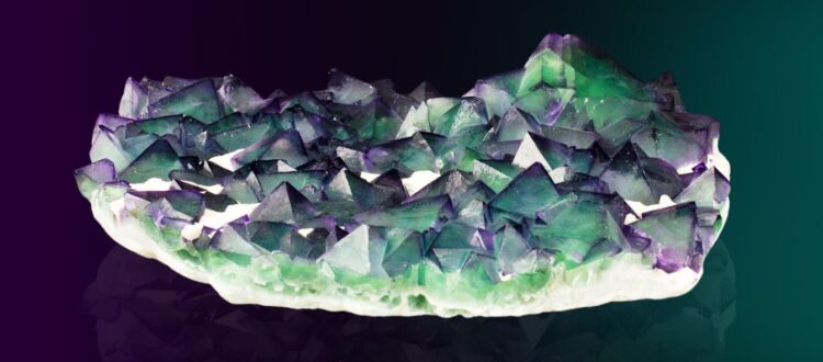 A vibrant cluster of green and purple crystals on a reflective surface.