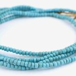 A multi-strand heishi beads necklace with a gold clasp on a white background.