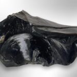 A large, shiny black raw obsidian stone with smooth, curved surfaces on a light background.