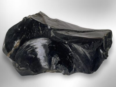 A large, shiny black raw obsidian stone with smooth, curved surfaces on a light background.