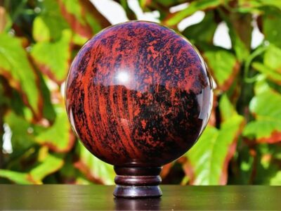 A polished red obsidian on a stand with green foliage in the background.