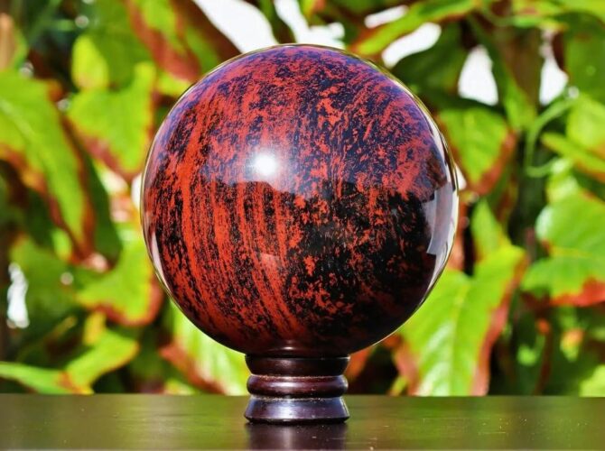 A polished red obsidian on a stand with green foliage in the background.